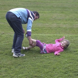 Father tickling his daughter on a lawn whilst his son watches on